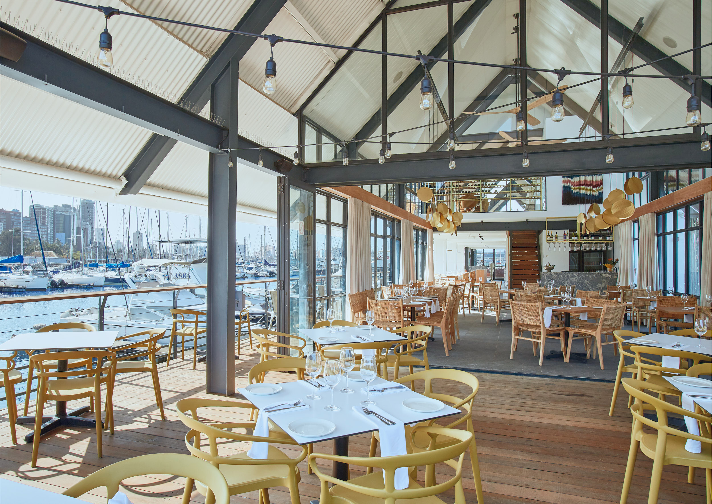 The waterside deck dining area, yellow bistro chairs and white-clothed tables, overlooking the marina